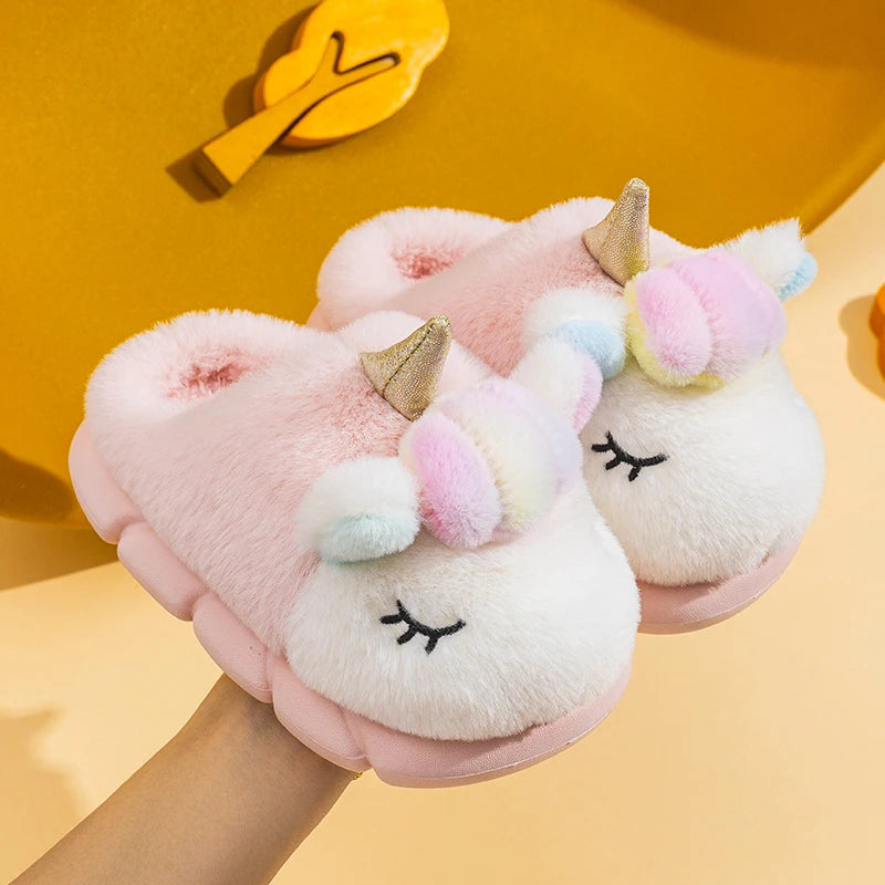 Pair of blush pink toddler unicorn plush slippers held in hand