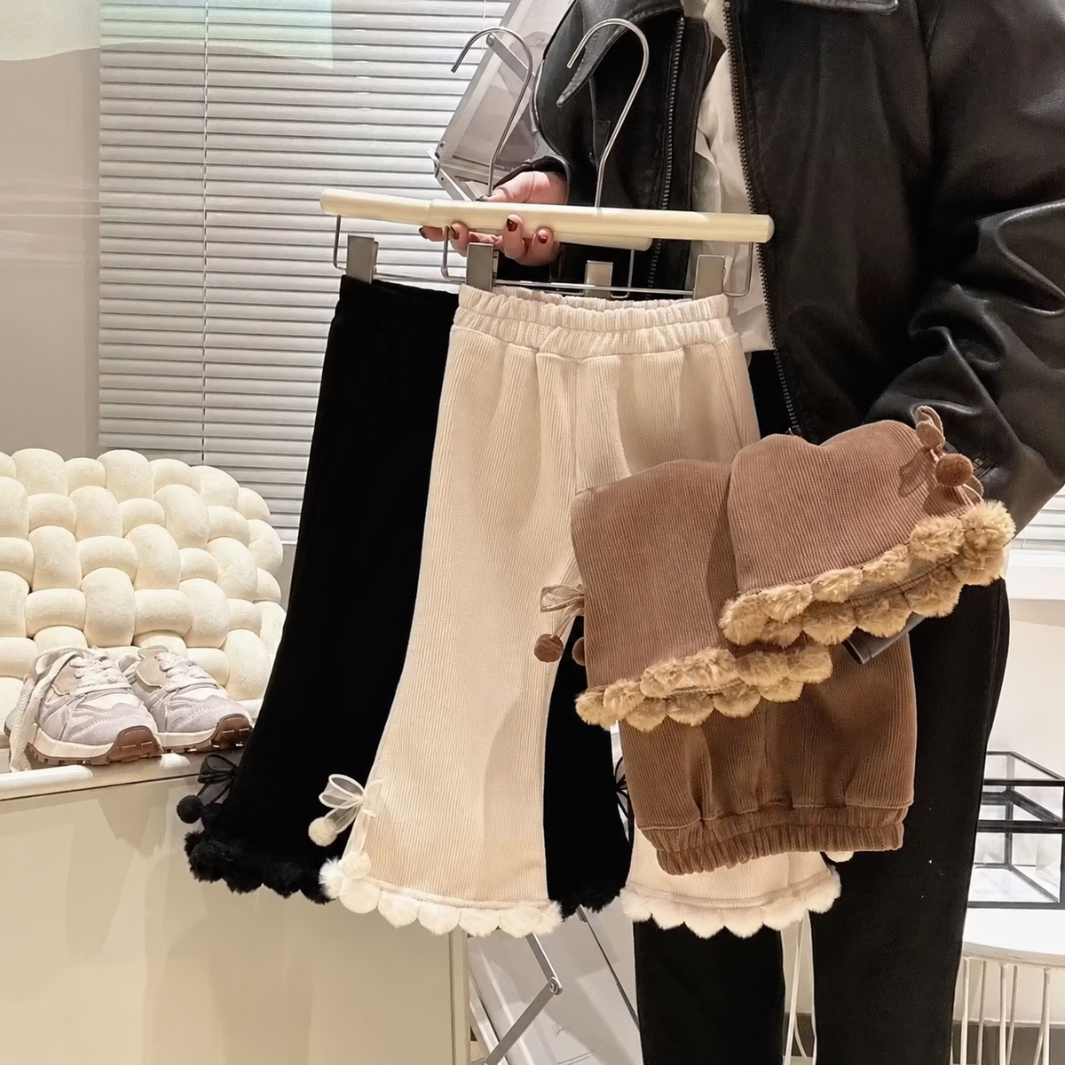 Three girls fleece-lined corduroy flare pants with pom-pom hems on a hanger